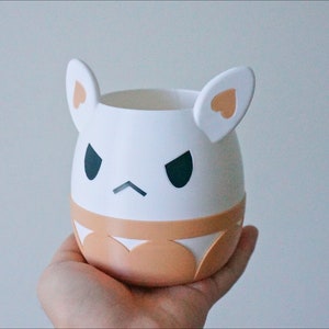 May include: White ceramic planter shaped like a cartoon animal with brown ears and a brown band around the middle. The animal has a grumpy expression with black eyes and a frown.