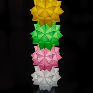 Pode incluir: Uma pilha de quatro estrelas de papel origami em amarelo, verde, rosa e branco. As estrelas est&atilde;o empilhadas umas sobre as outras, com a estrela amarela no topo e a estrela branca na parte inferior.