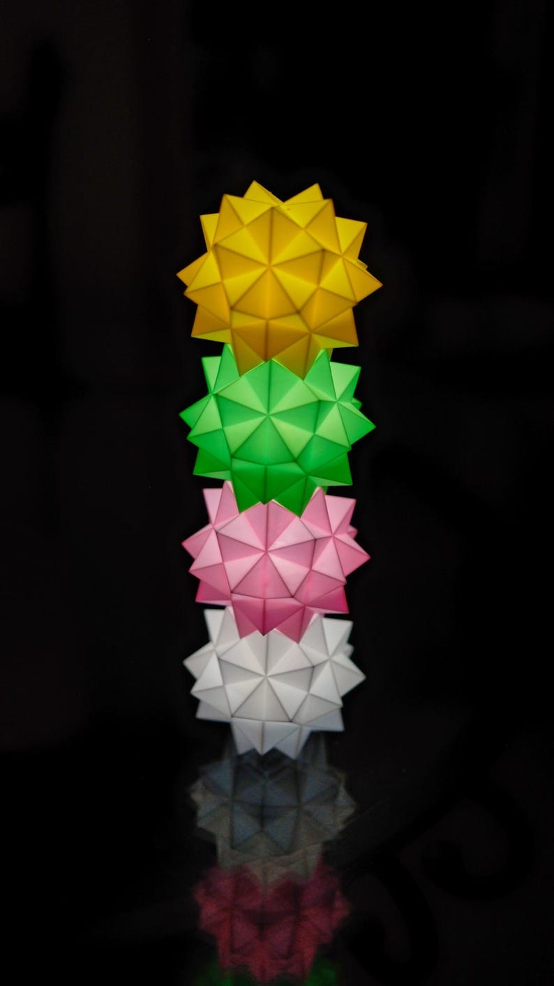 Pode incluir: Uma pilha de quatro estrelas de papel origami em amarelo, verde, rosa e branco. As estrelas est&atilde;o empilhadas umas sobre as outras, com a estrela amarela no topo e a estrela branca na parte inferior.