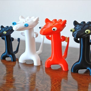 May include: Four whimsical dragon figurines in black, white, and red. Each dragon has a long neck, a tail, and large, expressive eyes. The figurines are displayed against a plain white background.
