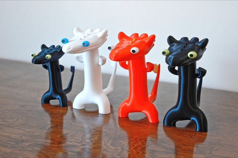 May include: Four whimsical dragon figurines in black, white, and red. Each dragon has a long neck, a tail, and large, expressive eyes. The figurines are displayed against a plain white background.