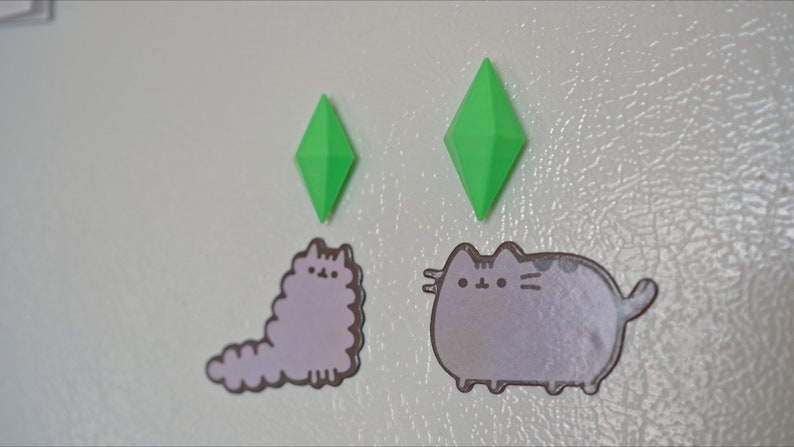 May include: Two green diamond-shaped magnets and two grey cat stickers on a white refrigerator.