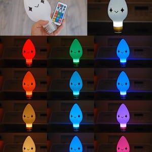 May include: A white, light-up bulb with a cartoon face and a remote control. The bulb's colour changes to red, green, blue, orange, yellow, and purple. The bulb has a standard base and a smiling face with diamond-shaped eyes.