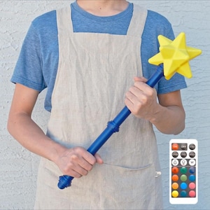 May include: A blue and yellow star-shaped wand with a remote control. The wand has a blue handle and a yellow star at the top. The remote control has several buttons with different colors.