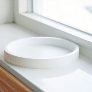 May include: A white ceramic round tray sits on a white windowsill.