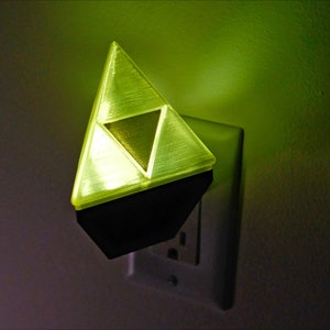 May include: A yellow plastic night light shaped like the Triforce from the Legend of Zelda video game series. The night light is plugged into a standard electrical outlet.