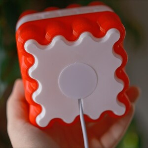May include: A red and white plastic toy with a white circle on the back. The toy has a wavy edge and a cord coming out of the white circle.
