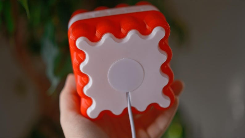 May include: A red and white plastic toy with a white circle on the back. The toy has a wavy edge and a cord coming out of the white circle.