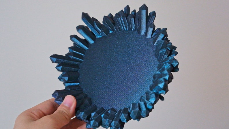 May include: A teal blue crystal-shaped dish with a round, flat interior. The dish is made of a textured material and has a unique, organic shape.