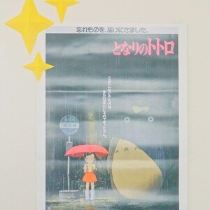 May include: A movie poster for the film "My Neighbor Totoro" featuring a young girl standing under a red umbrella in a rainy forest. The text on the poster reads "I forgot something, I came to deliver it. My Neighbor Totoro."