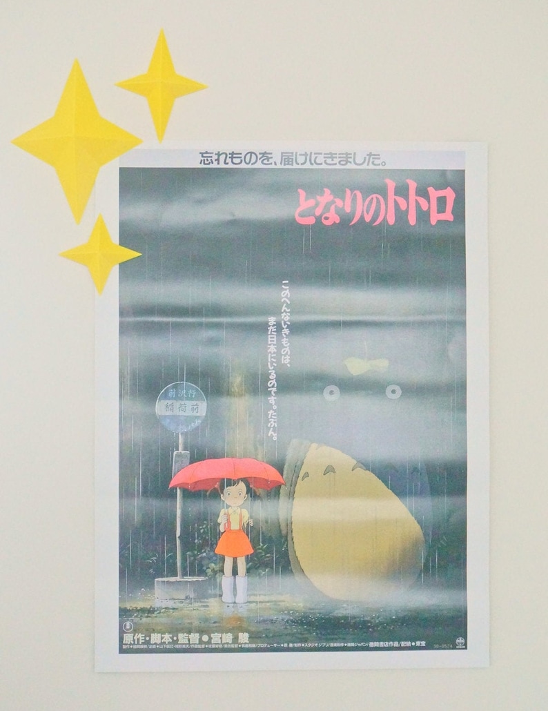May include: A movie poster for the film "My Neighbor Totoro" featuring a young girl standing under a red umbrella in a rainy forest. The text on the poster reads "I forgot something, I came to deliver it. My Neighbor Totoro."