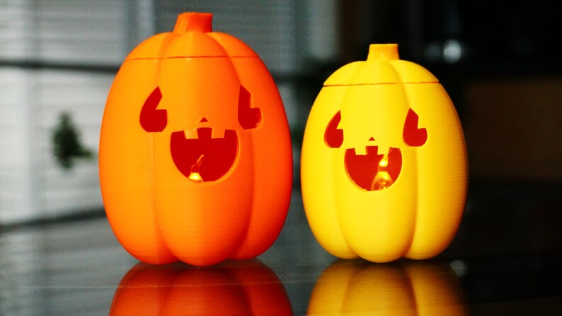 May include: Two Halloween jack-o'-lantern decorations, one orange and one yellow, with carved faces and lit from inside.