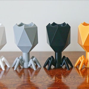 May include: Four geometrically shaped planters with a spider-like base. The planters are white, gray, black, and gold.