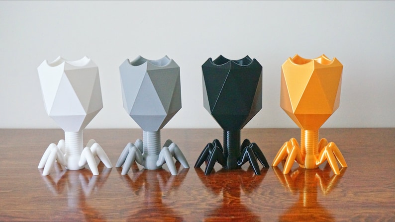 May include: Four geometrically shaped planters with a spider-like base. The planters are white, gray, black, and gold.