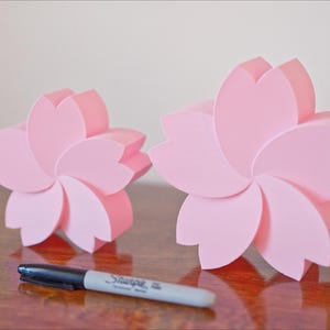 May include: Two pink ceramic flower-shaped boxes. The larger box is about 6 inches in diameter and the smaller box is about 4 inches in diameter.
