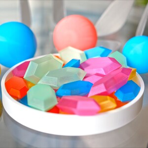 May include: A white bowl filled with colorful, translucent, geometric shapes. Three small, round, colorful objects with white wings are arranged around the bowl.