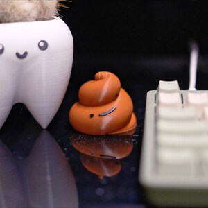 May include: A white tooth-shaped planter with a smiling face, a brown poop-shaped figurine with a smiley face, a pink bunny figurine holding a carrot, and a white keyboard with beige keys.
