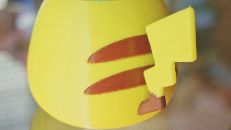 May include: A yellow Pikachu figurine with a brown lightning bolt tail. The figurine is made of plastic and has a smooth surface.