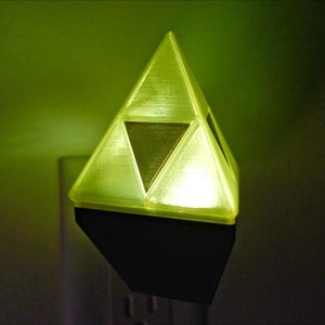 May include: A yellow triangular night light with a darker yellow triangle in the center. The night light is plugged into an electrical outlet.