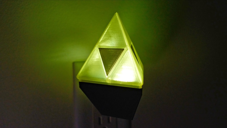May include: A yellow triangular night light with a darker yellow triangle in the center. The night light is plugged into an electrical outlet.