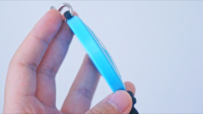 Puede incluir: Un llavero azul claro con un anillo de metal plateado y un cord&oacute;n negro.