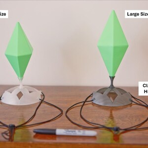 May include: Two decorative headpieces with green diamond-shaped tops and clear bases. One is white, the other black. The text on the image reads "Medium Size", "Large Size", "Clear White Headplate", and "Clear Black Headplate". A black marker is in the foreground.