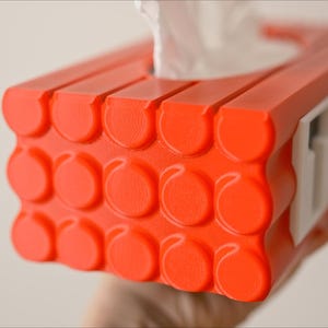May include: Orange tissue box holder with a white label that says "FREE". The holder is designed to look like a stack of building blocks.