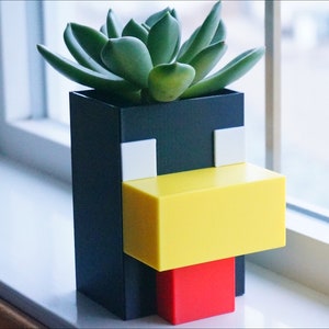 May include: A black and yellow 3D printed planter shaped like a Minecraft character with a green succulent plant inside.