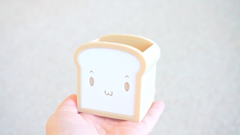 May include: A white and beige bread-shaped pencil holder with a cute cartoon face.