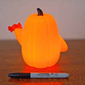 May include: A bright orange pumpkin-shaped night light with a red bow on the side. The light is on and glowing.
