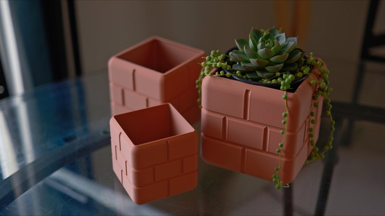 Pu&ograve; includere: Tre vasi di terracotta a forma di mattone, uno con una piccola pianta grassa. I vasi sono impilati uno sopra l'altro.