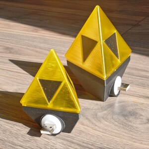 May include: Two yellow triangular shaped night lights with a black base and a USB plug. The lights are shaped like the Triforce from the Legend of Zelda video game series.