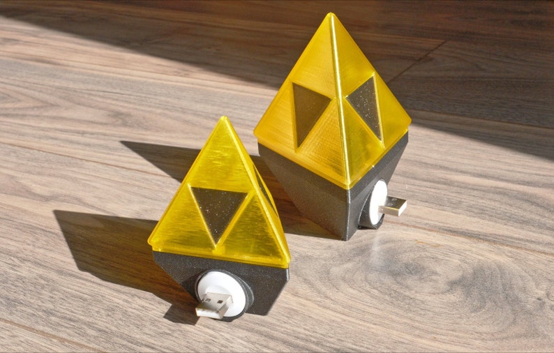 May include: Two yellow triangular shaped night lights with a black base and a USB plug. The lights are shaped like the Triforce from the Legend of Zelda video game series.