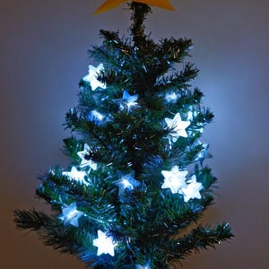 May include: A small artificial Christmas tree decorated with white star-shaped lights and a yellow paper star on top. The tree is in a black and silver planter.