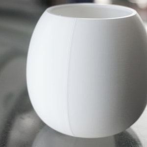 May include: A white ceramic vase with a smooth, rounded shape. The vase has a subtle seam down the side.