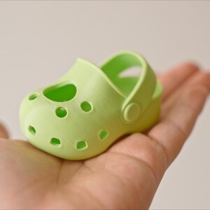 May include: A light green plastic clog with a strap and holes. The clog is small and appears to be for a child.