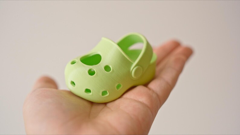 May include: A light green plastic clog with a strap and holes. The clog is small and appears to be for a child.