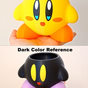 May include: Two 3D printed planters shaped like the character Kirby from the video game series Kirby. The first planter is yellow with blue eyes and a red mouth. The second planter is black with yellow eyes and a red mouth. Both planters have purple feet.