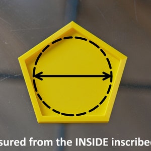 Op de afbeelding: Een gele onderzetter in de vorm van een vijfhoek met een zwarte gestippelde cirkel erin. De cirkel heeft een zwarte lijn erdoorheen met pijlen aan beide uiteinden. De tekst "Size measured from the INSIDE inscribed circle" staat onder de onderzetter.