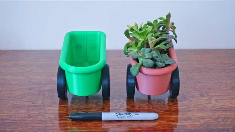 May include: Two small green and terracotta planters on wheels, each with a different type of succulent plant. The planters are on a wooden surface with a black marker pen.