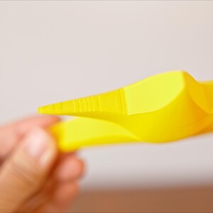 May include: A yellow plastic star-shaped object with a pointed tip. The object is held in a person's hand.