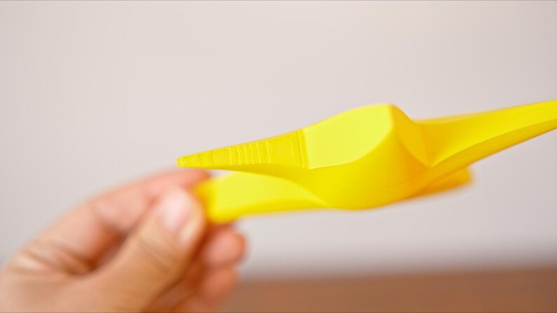 May include: A yellow plastic star-shaped object with a pointed tip. The object is held in a person's hand.