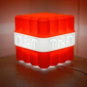 Puede incluir: Una luz roja y blanca con forma de bloque de TNT con las palabras "GET THAT" en el lado blanco.