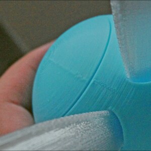 Puede incluir: Una esfera azul claro impresa en 3D con tres alas blancas impresas en 3D unidas a ella.