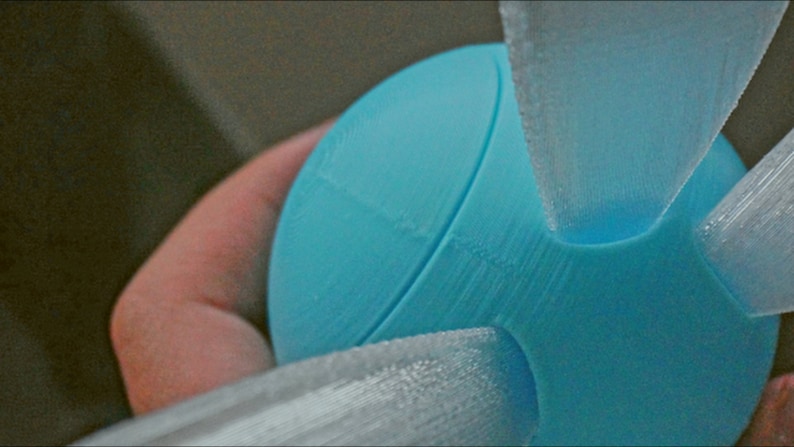Puede incluir: Una esfera azul claro impresa en 3D con tres alas blancas impresas en 3D unidas a ella.