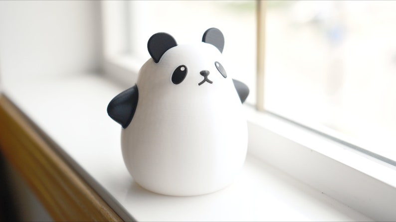 Op de afbeelding: Een wit keramiek panda-beeldje met zwarte oren, ogen, neus en mond. De panda staat op een wit oppervlak.