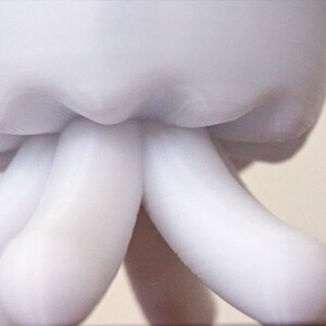 May include: White ceramic sculpture of a head with two long, rounded arms extending downwards.