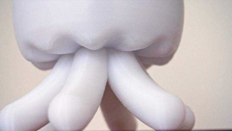 May include: White ceramic sculpture of a head with two long, rounded arms extending downwards.