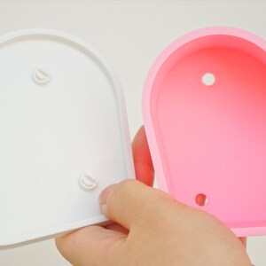 Puede incluir: Dos macetas en forma de coraz&oacute;n, una blanca y otra rosa. Ambas macetas tienen tres peque&ntilde;os agujeros en la parte inferior.