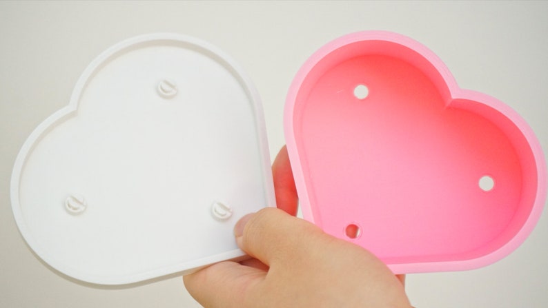 Puede incluir: Dos macetas en forma de coraz&oacute;n, una blanca y otra rosa. Ambas macetas tienen tres peque&ntilde;os agujeros en la parte inferior.